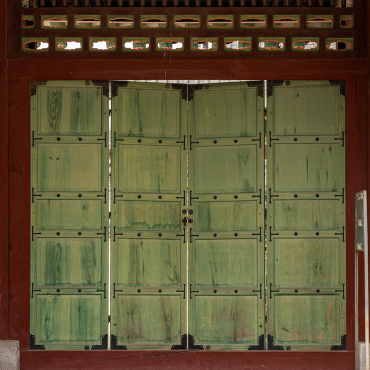 Traditional wooden folding doors at Changdeokgung Palace in Seoul, featuring green-paneled wood with intricate iron hinges and decorative dancheong patterns, typical of Joseon-era royal architecture.