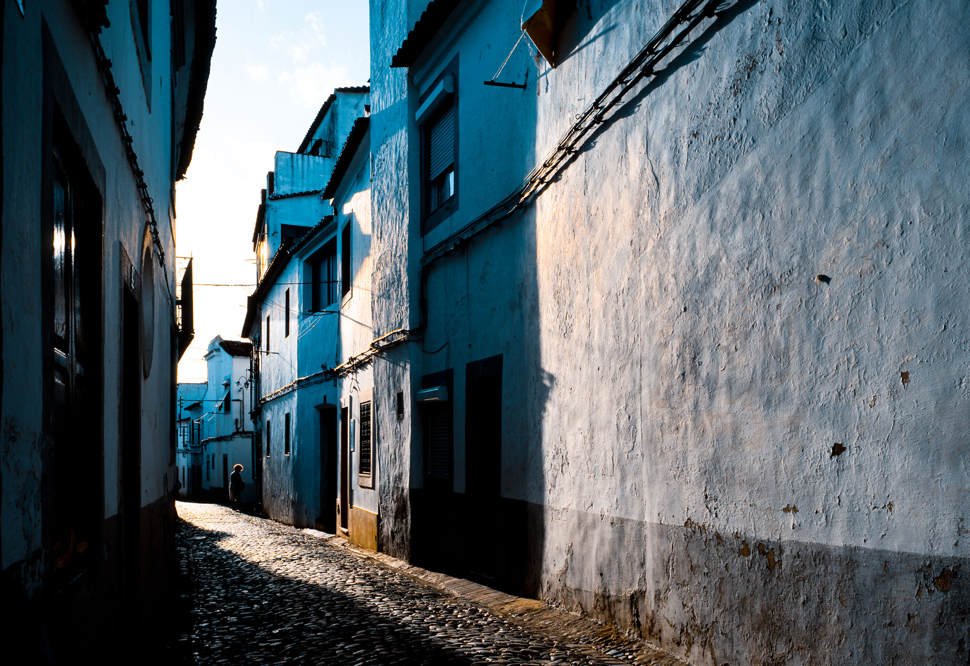 Photograph of Evora, Portugal in the early morning. An old cobblestone alley.
