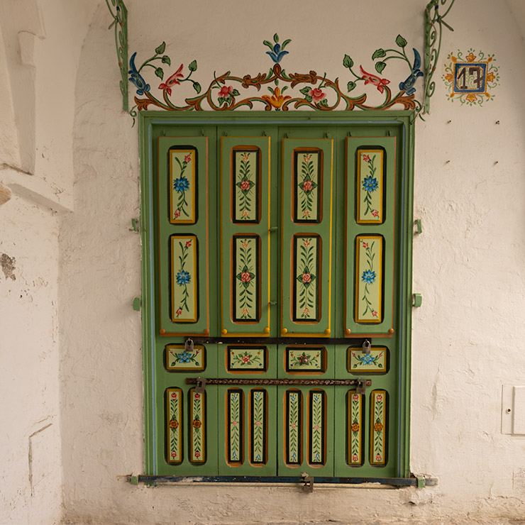 Ornate green wooden door with floral hand-painted panels and decorative ironwork in the Medina of Tunis.