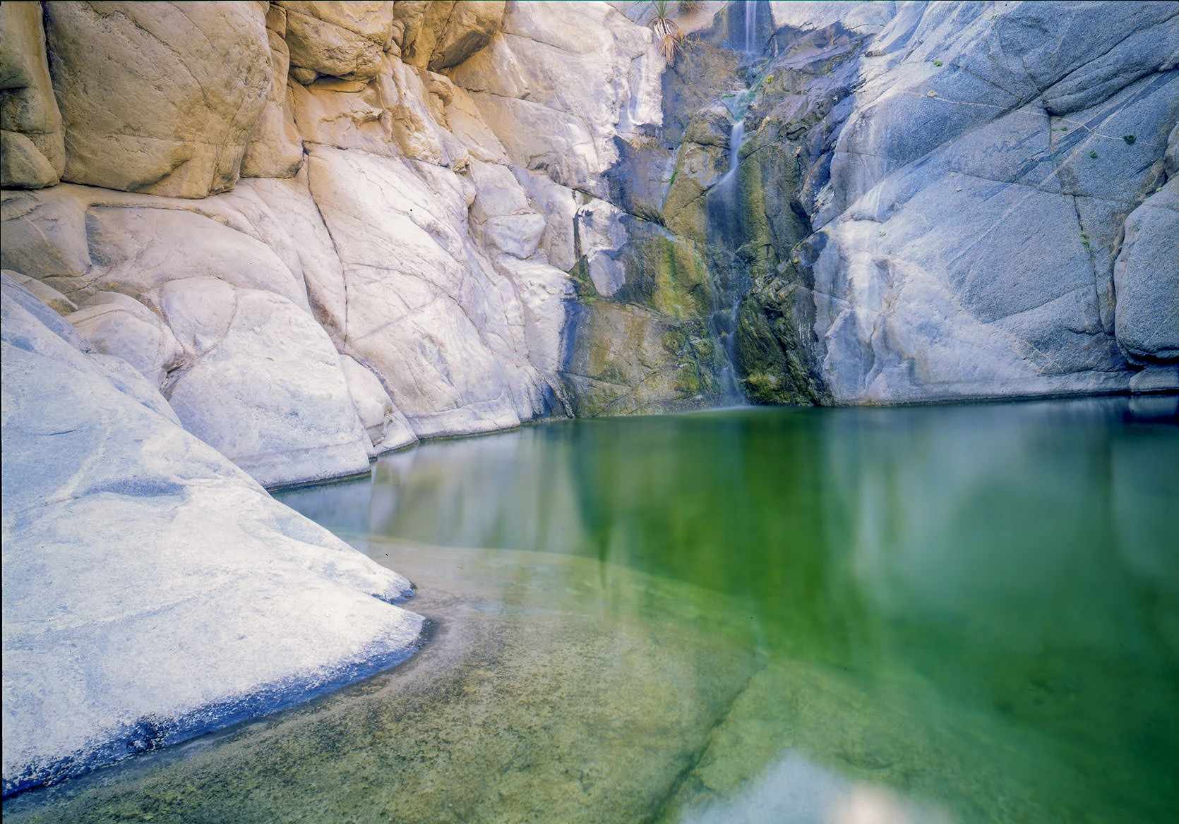 Natural rock pool in Guadalupe Canyon, Baja California, surrounded by desert cliffs and palms. Fed by hot springs, these pools are a hidden oasis where travelers camp and soak in the midst of rugged wilderness.