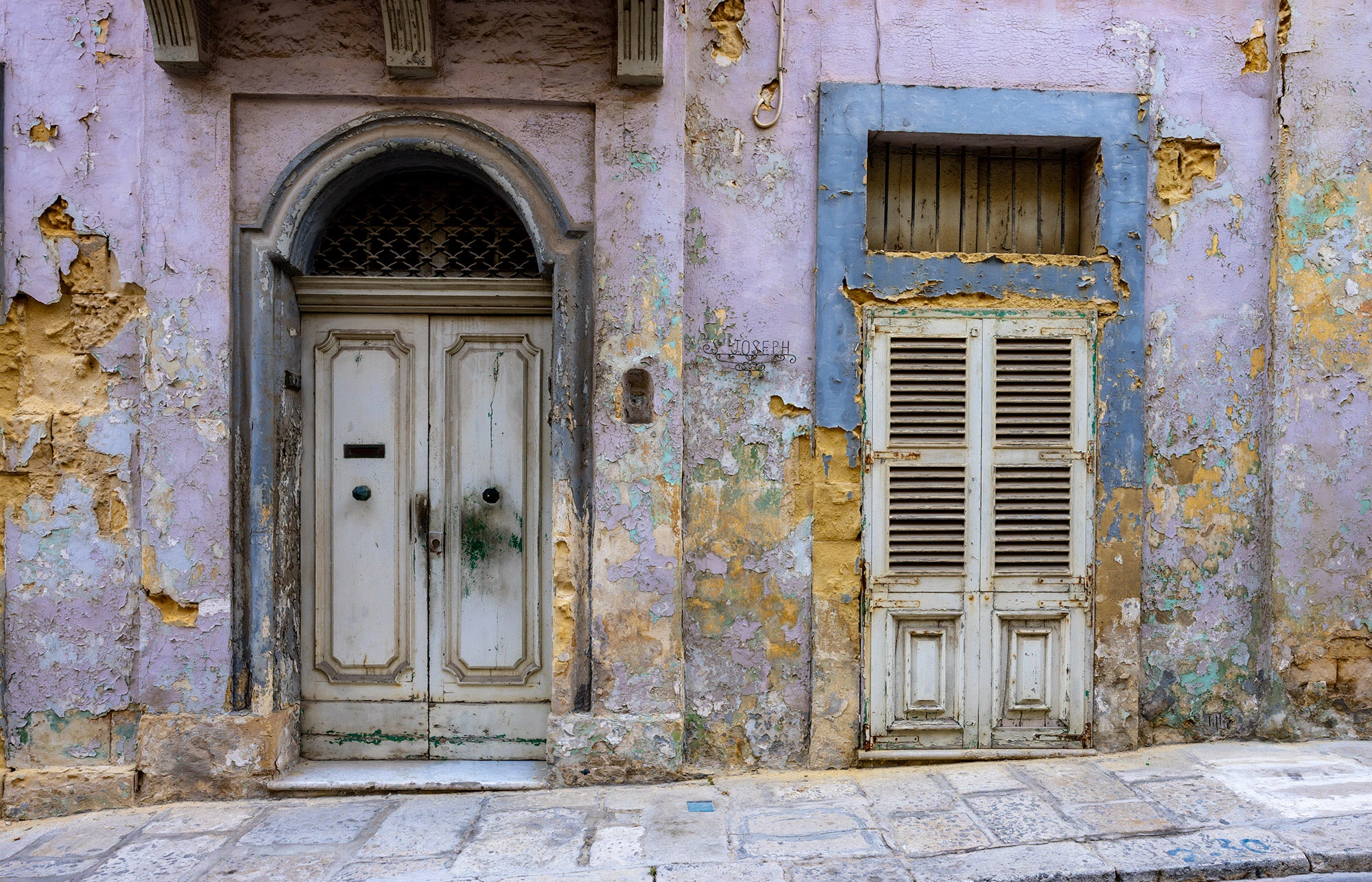 A pair of weathered doors in Birgu, Malta, their peeling layers of lavender, ochre, and blue paint revealing centuries of wear and change.