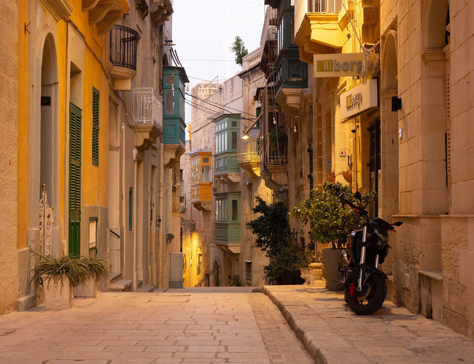 Morning view of the historic Birgu waterfront in Malta, with honey-colored limestone buildings reflecting in the calm harbor. A single boat is moored in the foreground, while the narrow streets and fortified walls rise behind, capturing Malta's blend of Mediterranean and medieval charm.