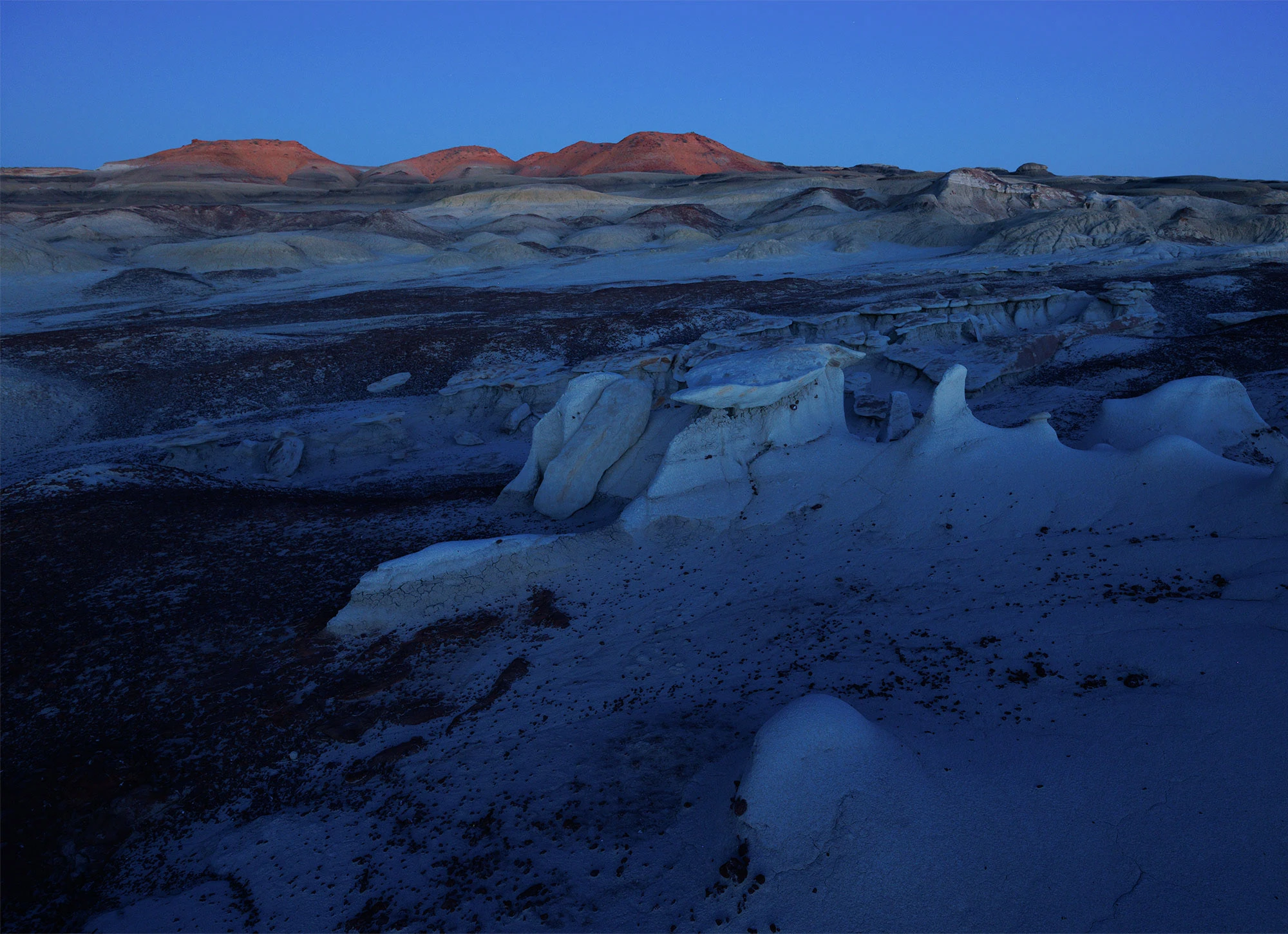 Blue twilight over sculpted badlands in the Bisti/De-Na-Zin Wilderness, with distant red mesas faintly lit by the last light of day.