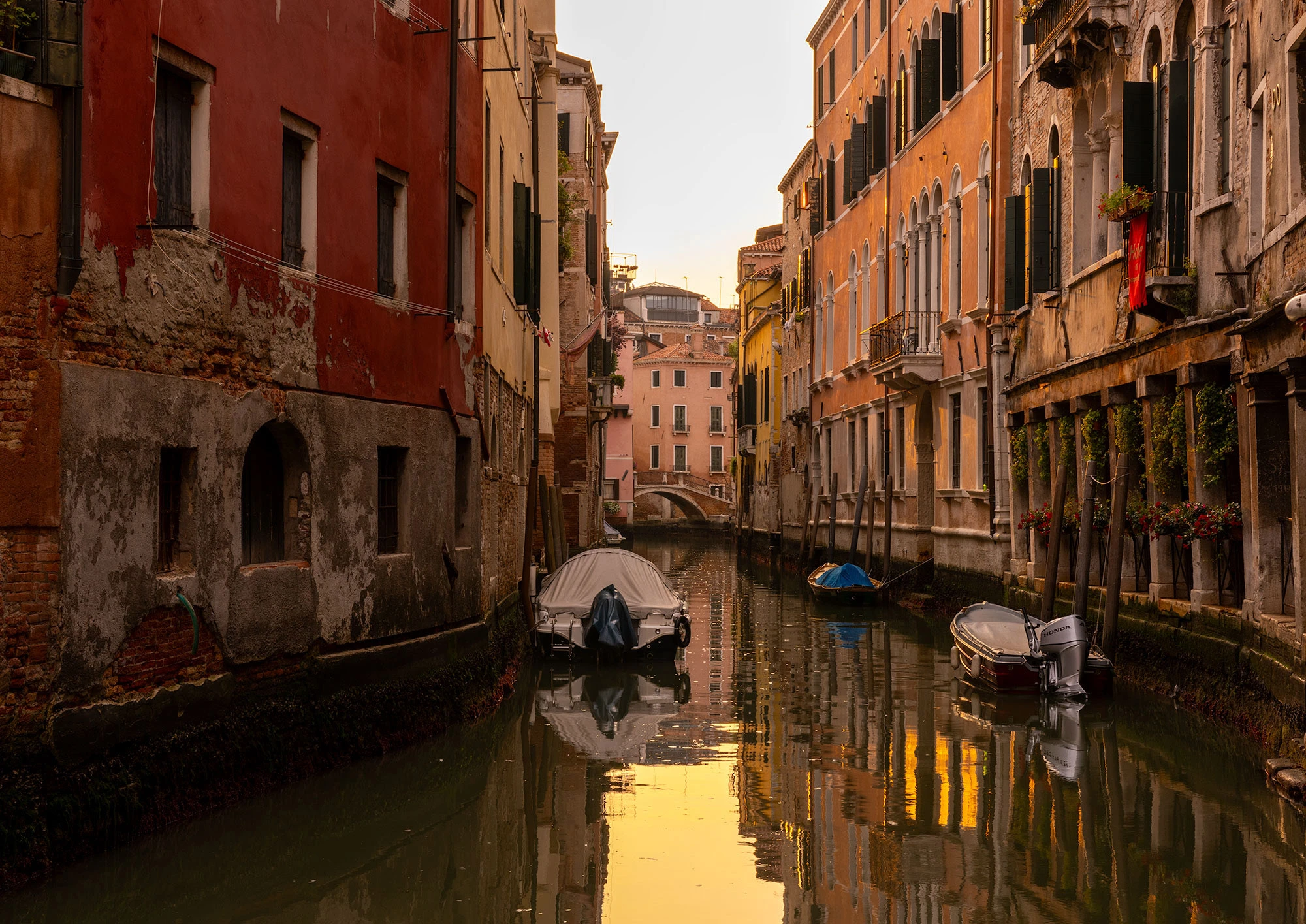 A tranquil, predawn canal in Venice's Cannaregio neighborhood, flanked by dimly lit buildings and reflected lights in the still water.
