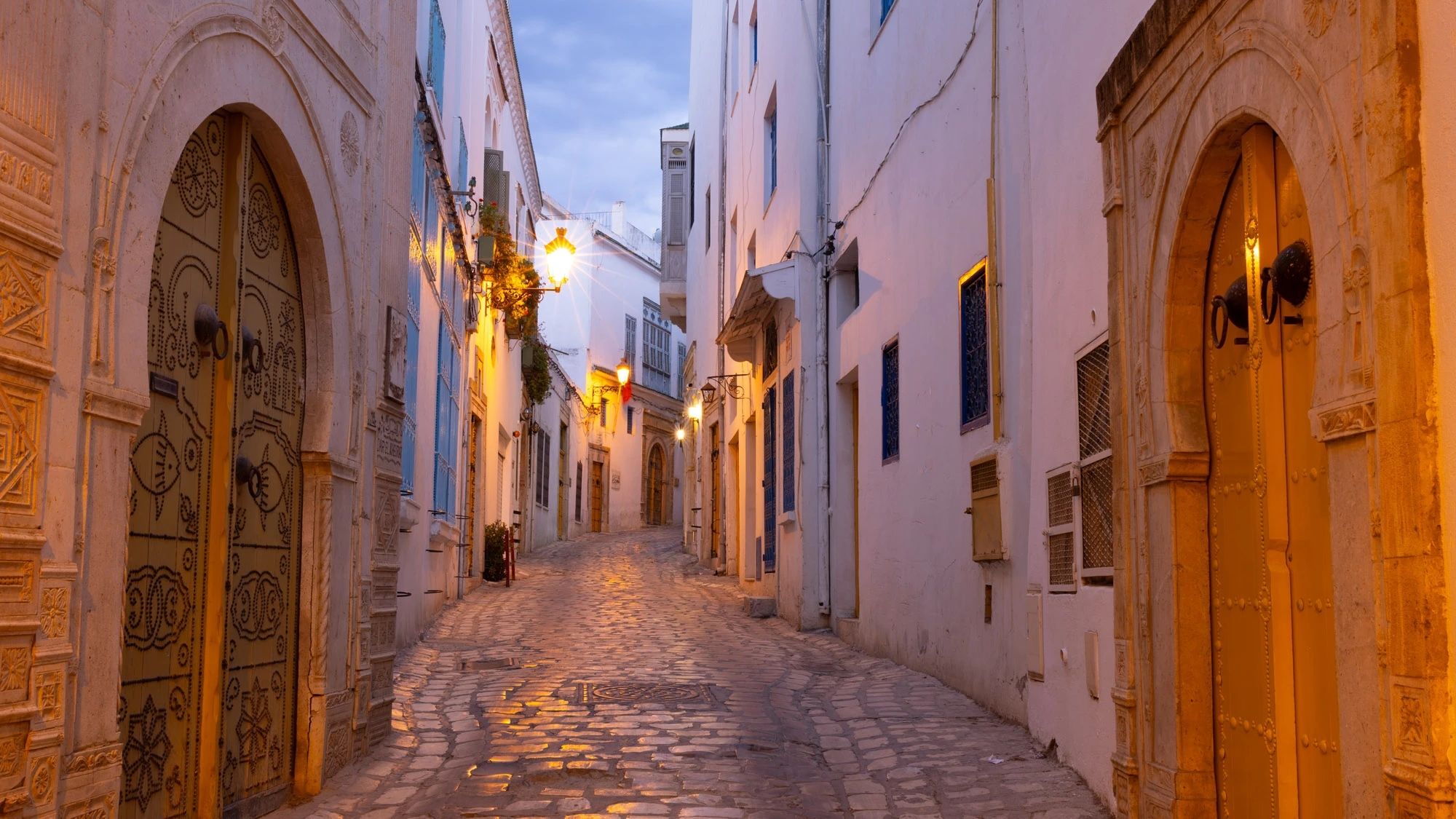 Narrow dusk alley in Rovinj, Croatia—warm stone walls, glowing windows and lantern light, polished cobbles tapering toward the sea—an invitation to wander and discover Europe.