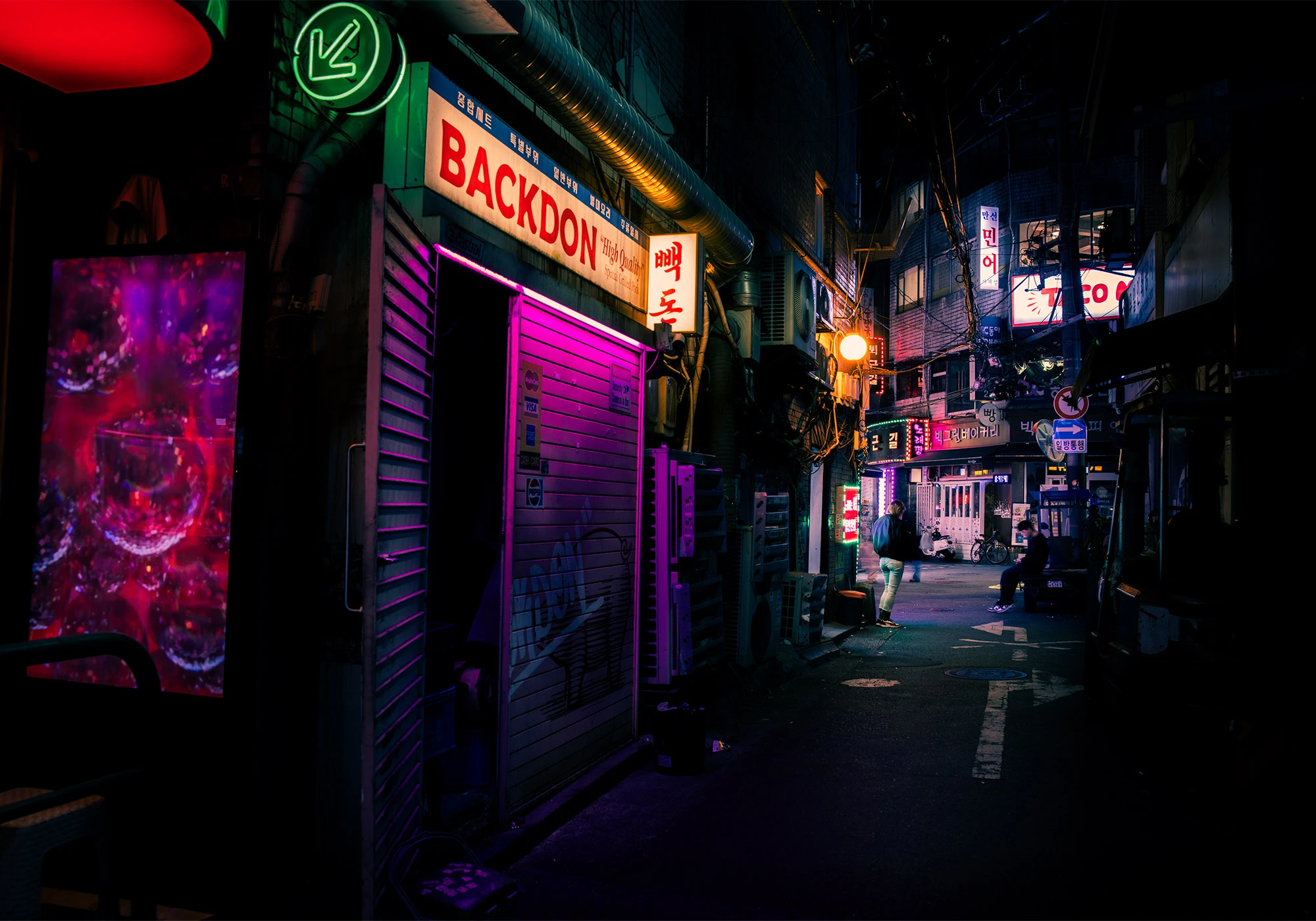 A narrow alley in Seoul's Jung District glows with neon lights at night, featuring the entrance to Backdon Korean BBQ with a half-open metal shutter bathed in magenta and green light. Surrounding the restaurant are vibrant digital displays, tangled wires, and Korean signs stacked along the buildings, while a few shadowy figures walk under the moody, color-soaked glow.