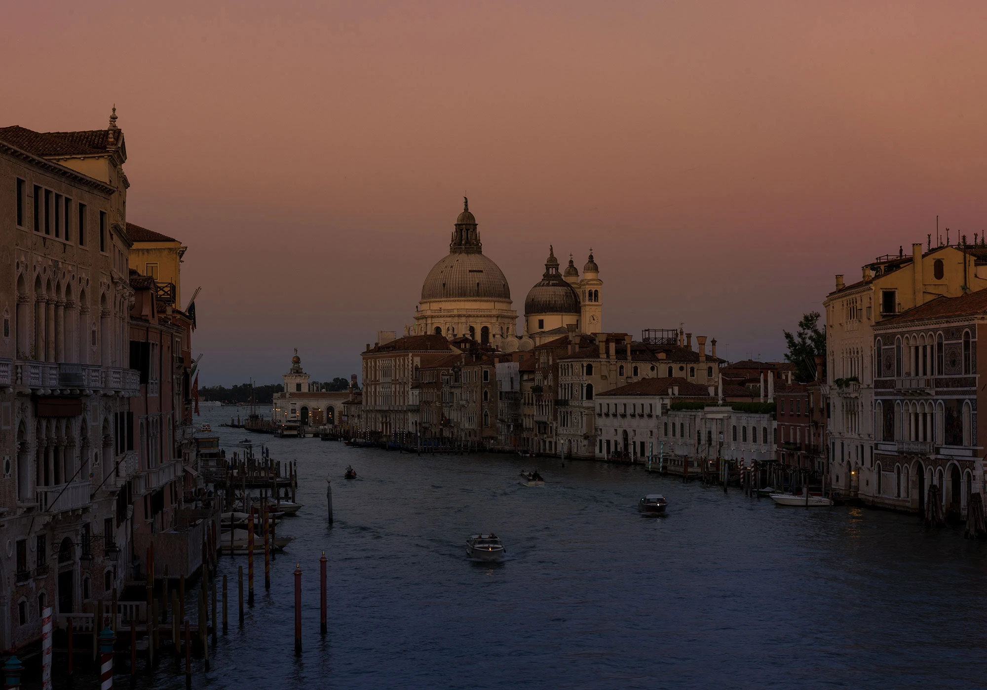 The Venice Grand Canal is lined with historic, colorful buildings and filled with boats at predawn, creating a vibrant and bustling waterway scene.