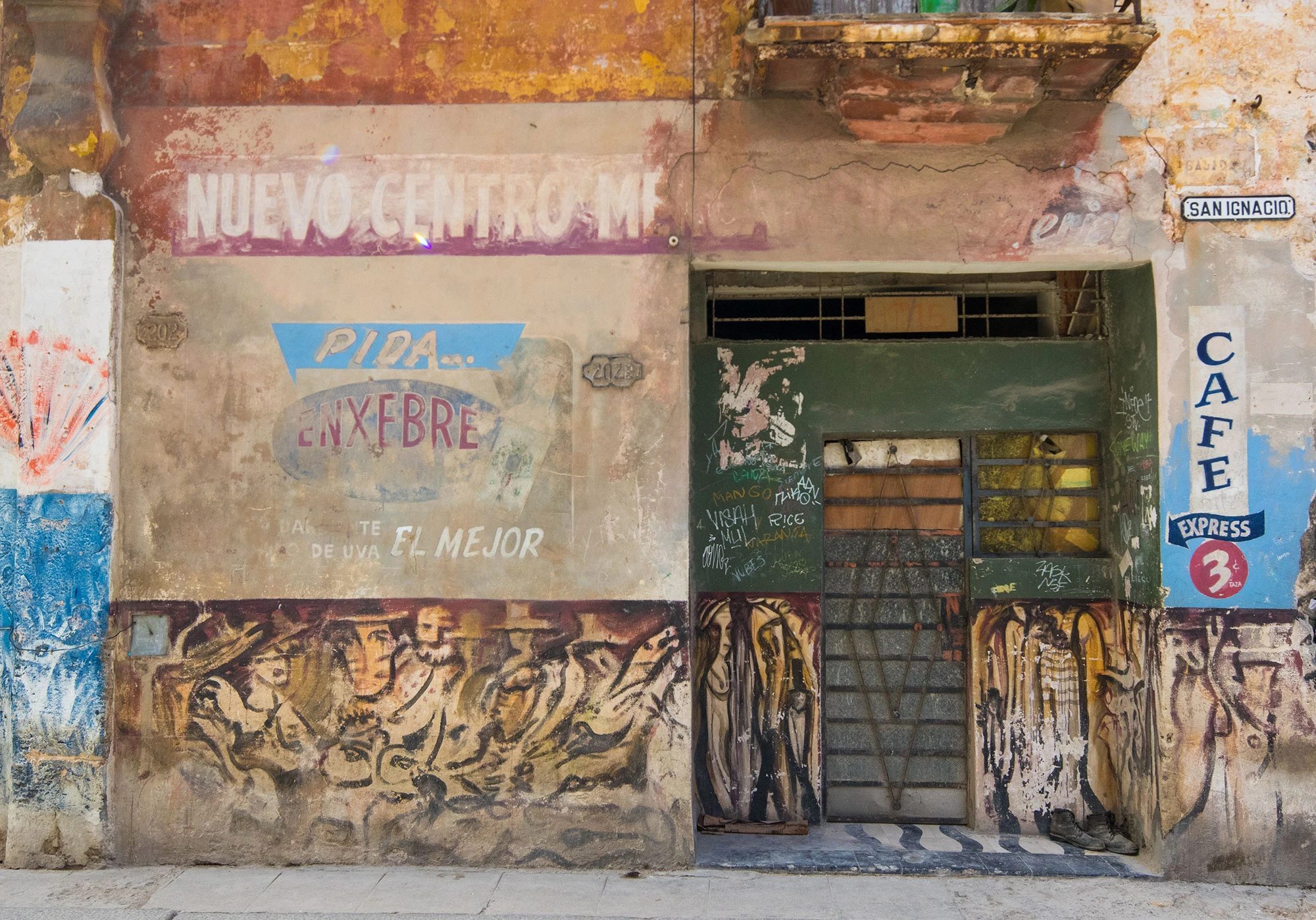A weathered wooden door in Habana Vieja, Cuba, covered in colorful street art and graffiti, framed by peeling stucco walls that hint at the city's layered history and vibrant artistic spirit.