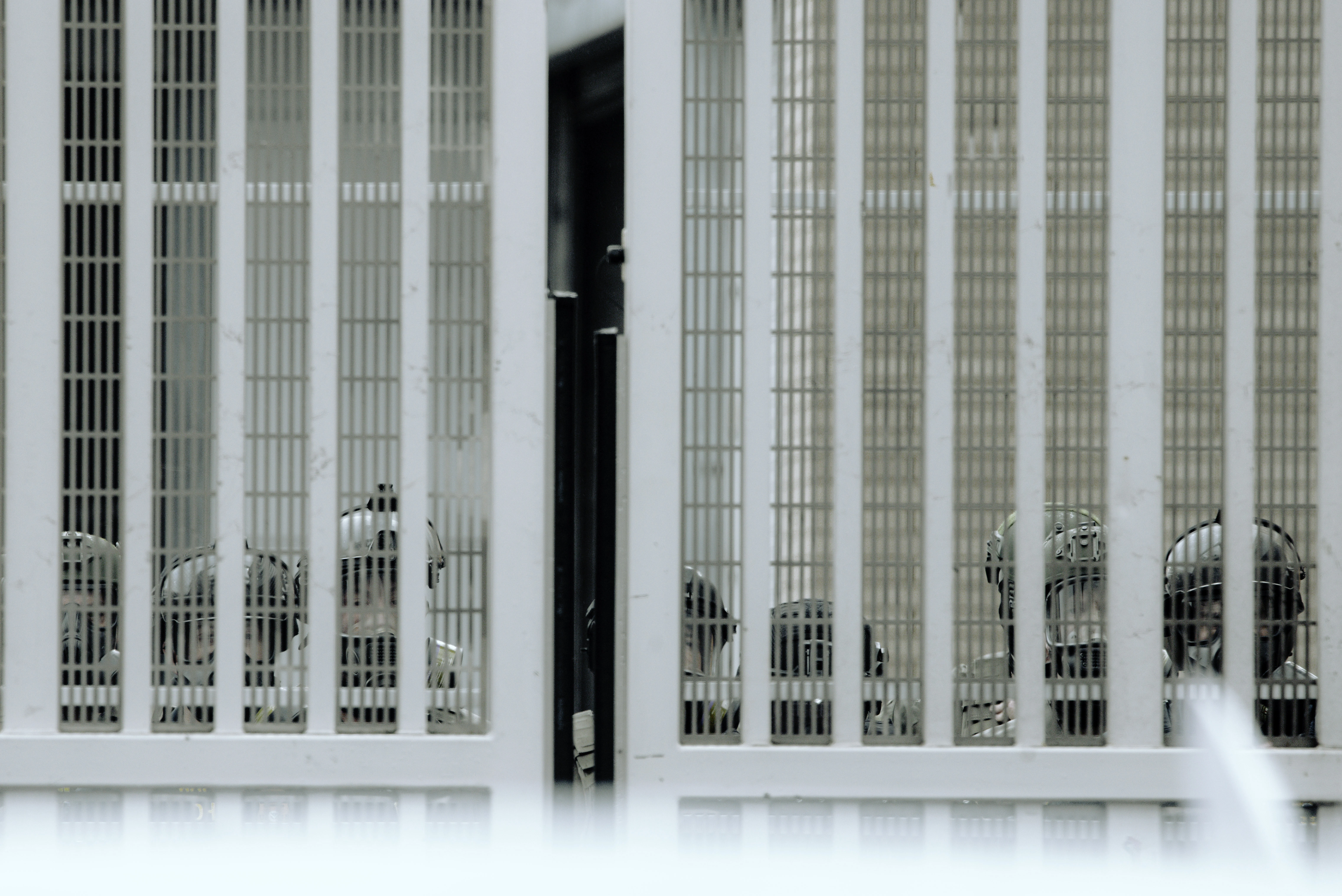 Behind the steel gates of Portland's ICE building, helmeted federal agents stare outward toward the protesters gathered outside, their faces partially obscured by the bars in a chilling scene of confrontation and division.