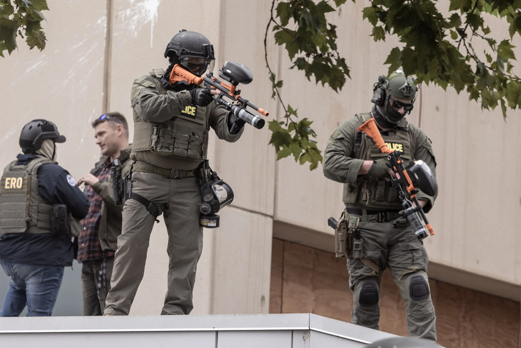 Department of Homeland Security police officers stand on the roof of Portland's ICE building, aiming pepper ball launchers at peaceful protesters below during the city's demonstrations against federal enforcement.