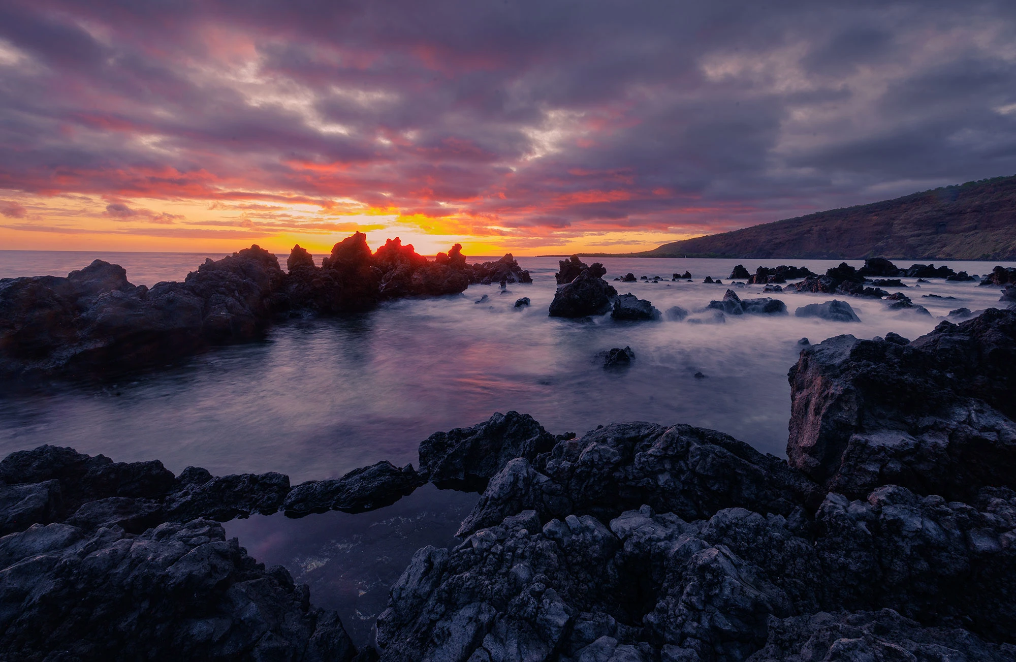 Kealakekua Bay at last light, with glassy water reflecting purple twilight beneath towering cliffs where forest meets reef. The calm surface hints at deep cultural memory and ecological richness in this Marine Life Conservation District.