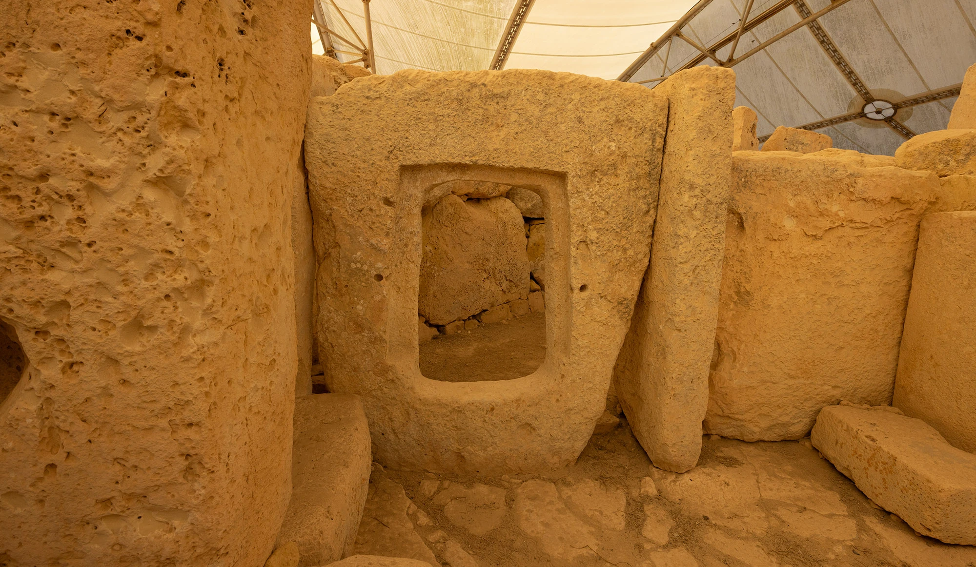 Rectangular stone doorway carved into a massive limestone slab inside the Neolithic temple complex of Ħaġar Qim, Malta, with an opening leading to an interior chamber under a protective canopy.