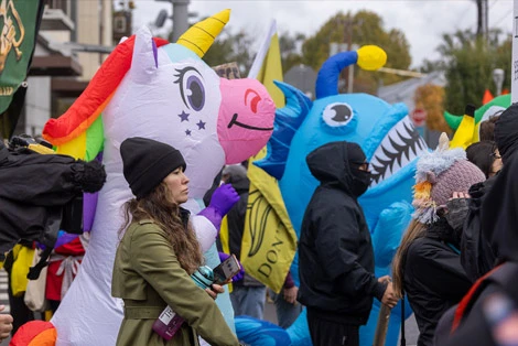 Protesters in Portland wear colorful costumes, including a unicorn and shark, while marching against ICE outside the federal building.