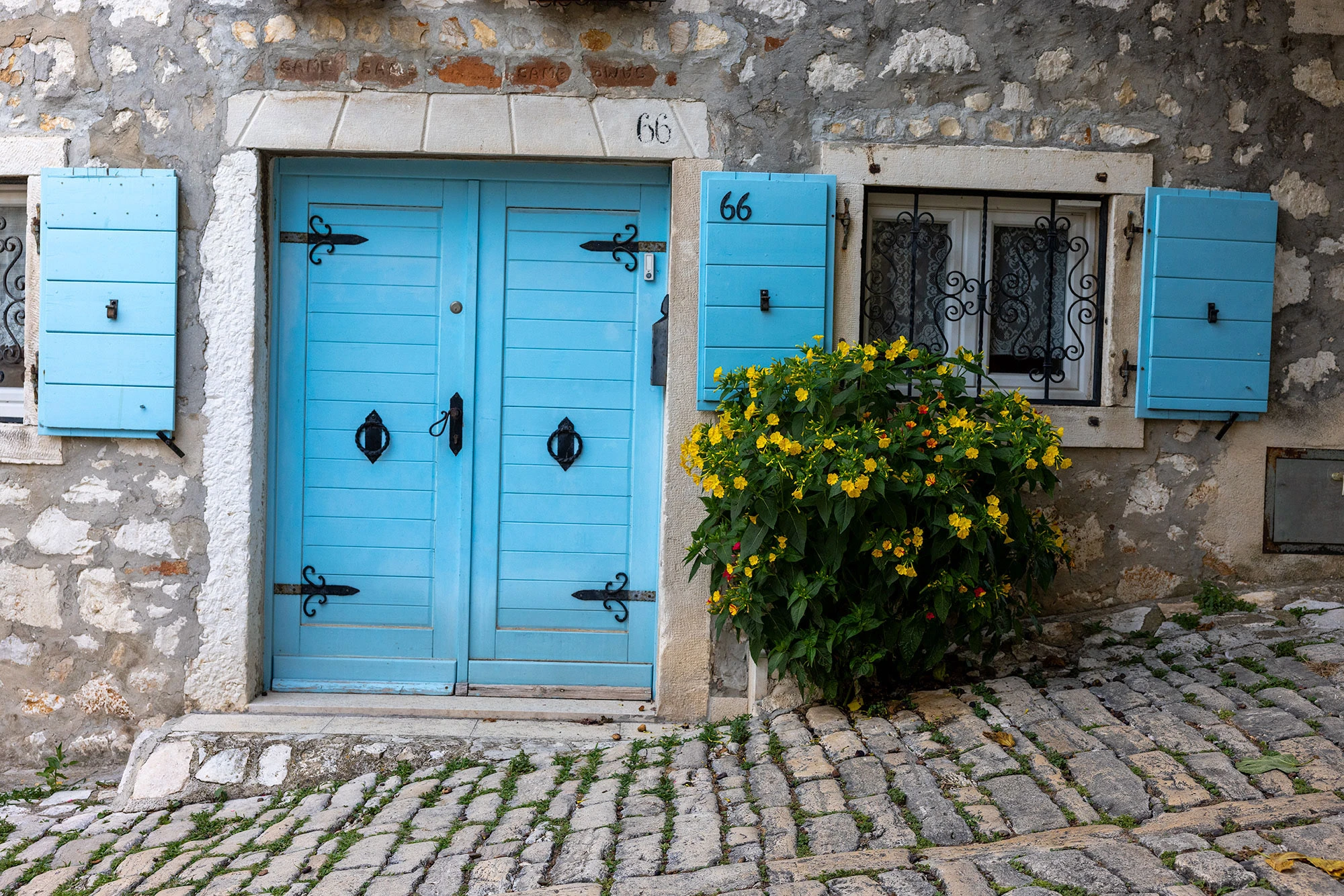 A predawn scene in Rovinj with a weathered door and shuttered window, both blue, set in an old, peach-colored wall under soft light.