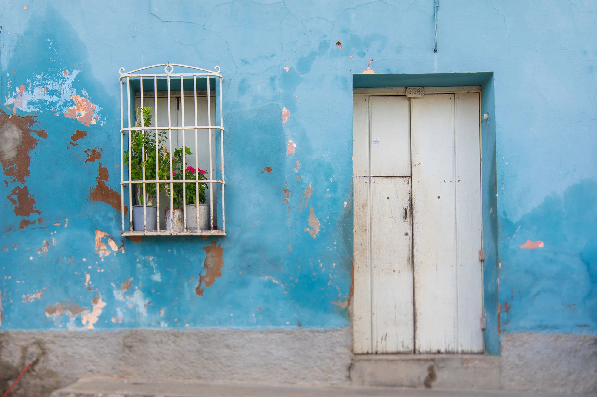 Door and typical wrought-iron window in Trinidad, Cuba, their weathered pastel walls and iron grilles reflecting the town's Spanish colonial craftsmanship and tropical patina.
