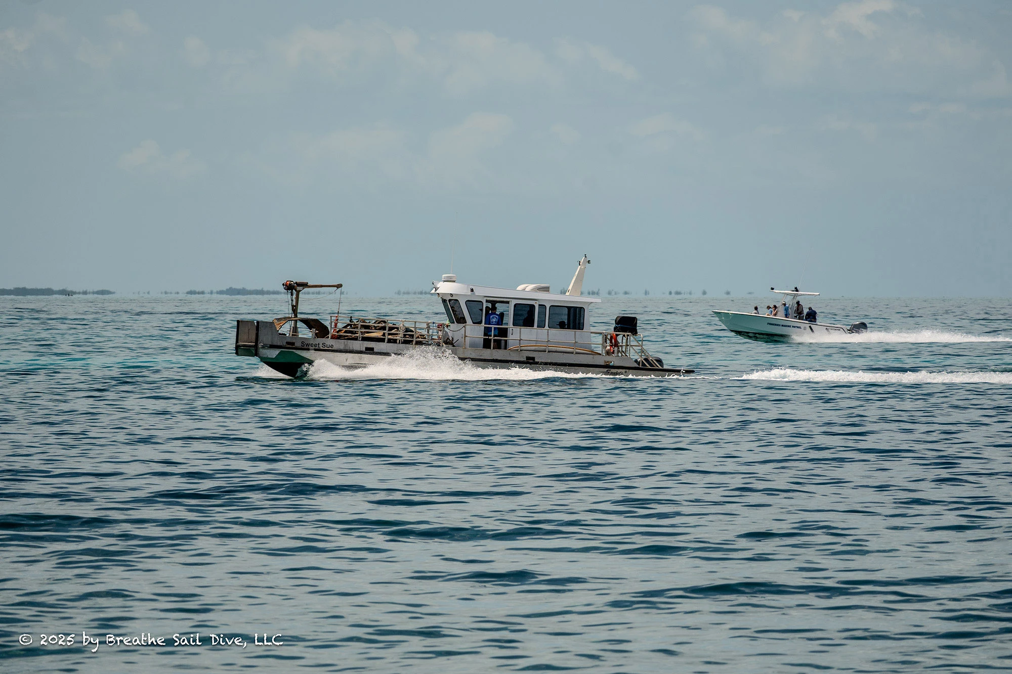 Two boats speed across calm, clear waters near Fowl Cays National Park. In the foreground, a workboat labeled 
